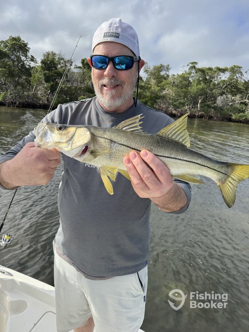 Angler proudly displaying a Snook caught while fishing in a scenic coastal environment.