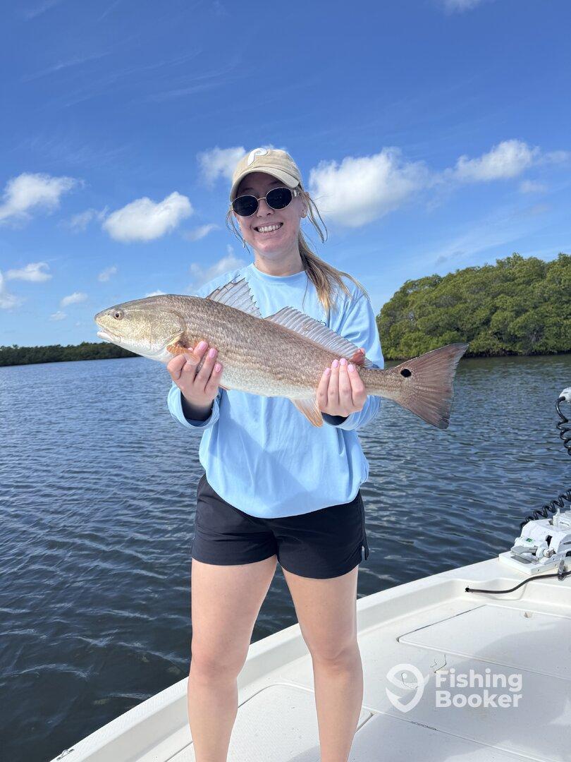 A young angler proudly displaying a Redfish while fishing in a scenic coastal environment.