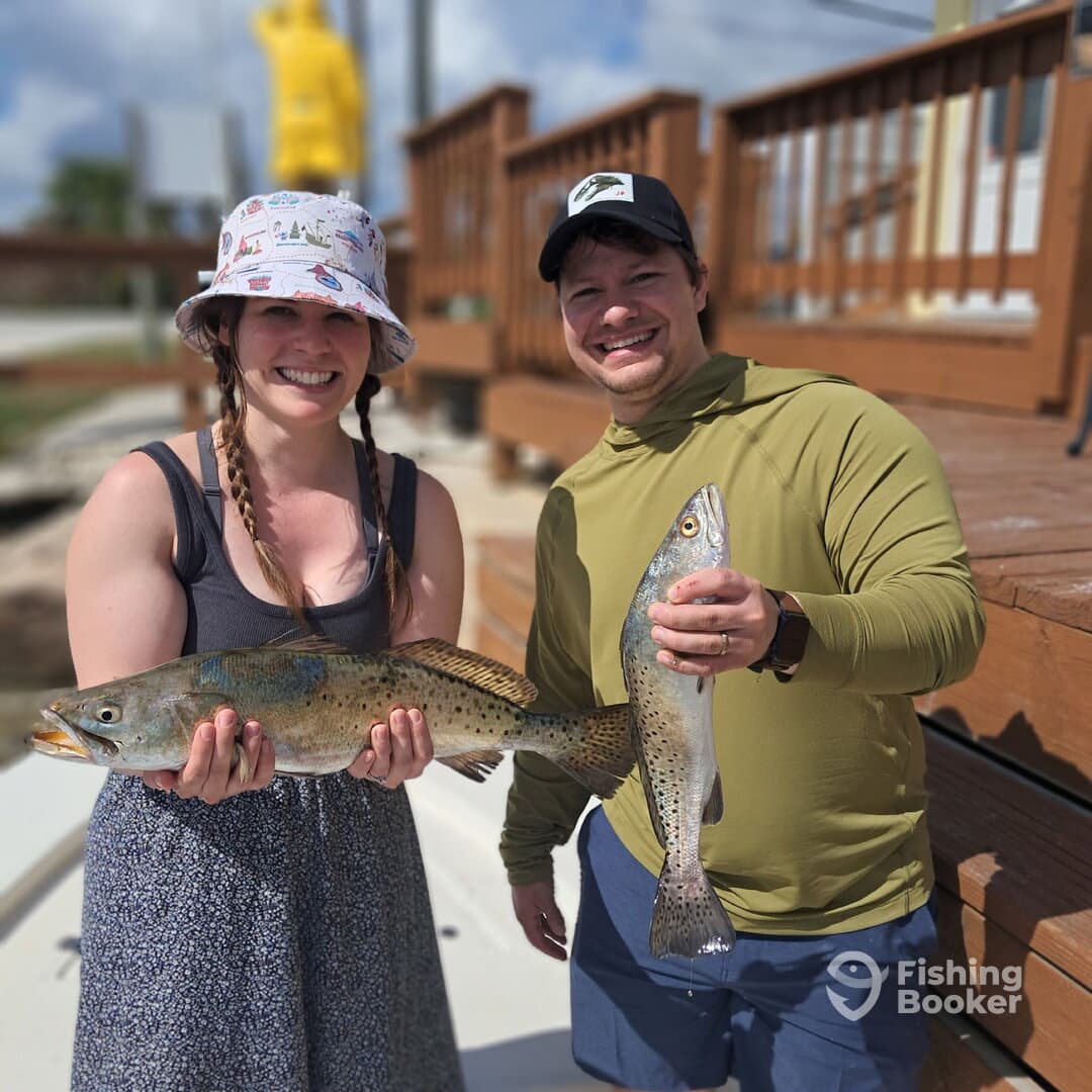 Two anglers proudly displaying their catch of Speckled Trout at the dock, showcasing a successful fishing trip.