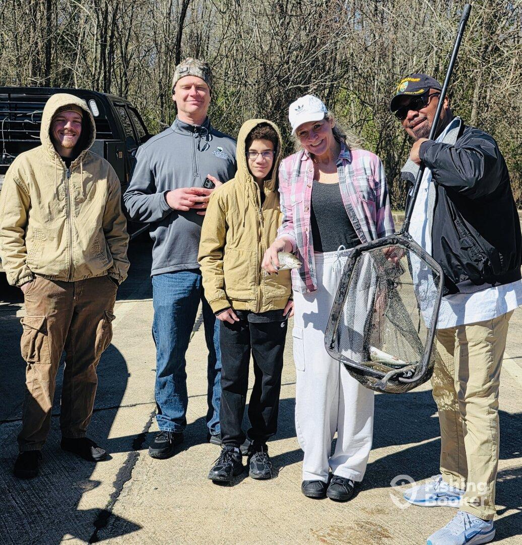 A family poses proudly with their catch, showcasing a net with several fish after a successful fishing trip.