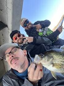 Three anglers posing with a freshly caught Crappie while enjoying a day of fishing on the water.