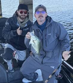 Two anglers proudly displaying a large Crappie while fishing from a boat, showcasing a successful day on the water.