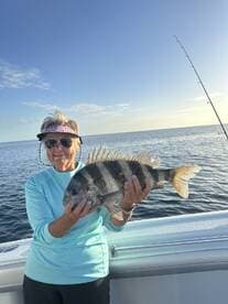A proud angler holding a large Black Sea Bass while fishing on a sunny day at sea.