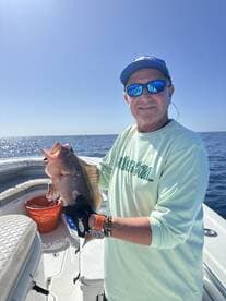 Angler proudly displaying a large Grouper while fishing on a sunny day in open waters.