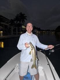 Angler proudly displaying a Snook caught during a night fishing trip in a scenic canal.