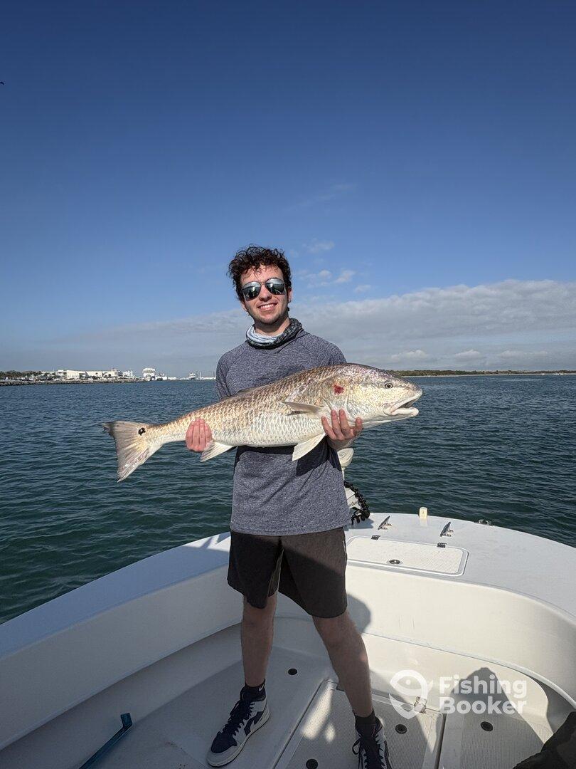 Angler proudly displaying a large Redfish on a boat during a fishing trip.