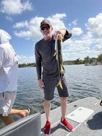A proud angler holding a Snook while fishing on a sunny day in a scenic waterway.