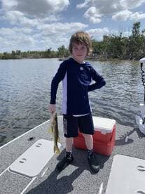 Young angler proudly holding a Snook while fishing on a boat in a scenic waterway.