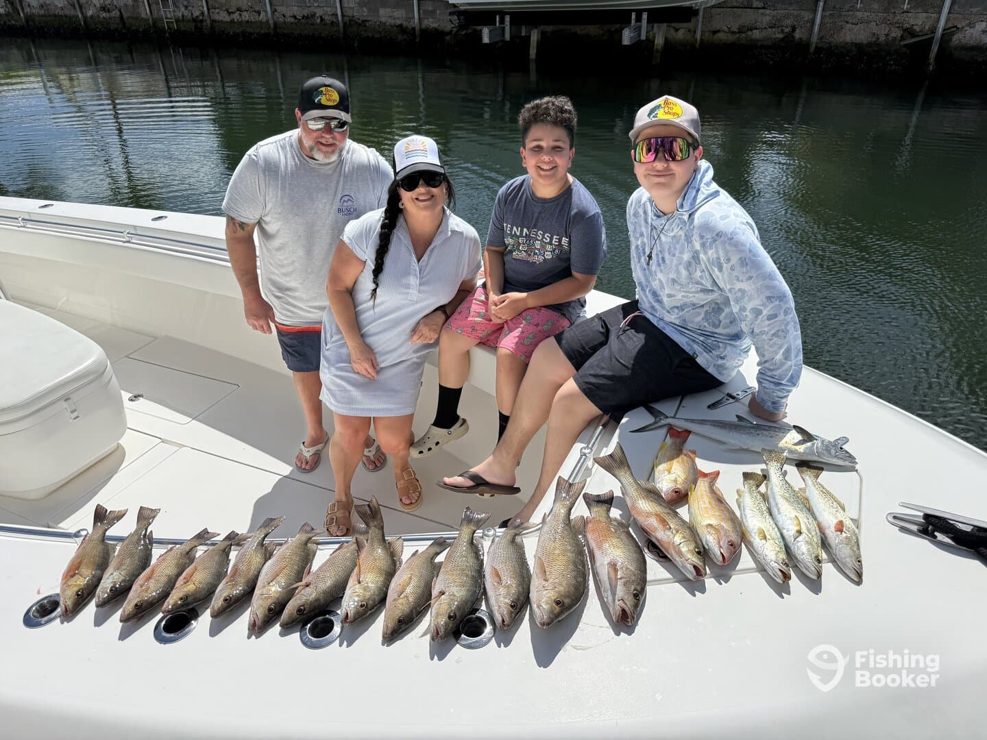 A family poses on a boat with a successful catch of various fish, including redfish and trout, displayed neatly along the side.