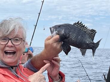 An excited angler proudly displaying a Black Sea Bass while fishing offshore, showcasing the joy of a successful catch.