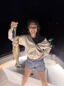 Angler proudly displaying a Snook caught during a night fishing trip on a boat.