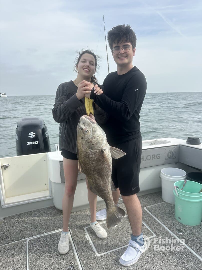 Two young anglers proudly displaying a large Grouper caught during a fishing trip on a boat.