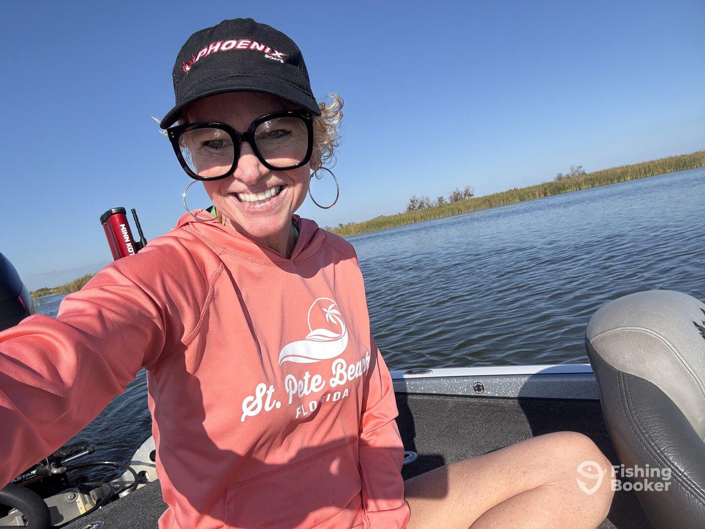 A smiling angler on a Phoenix boat, enjoying a sunny day on the water, showcasing the comfortable seating and scenic backdrop.