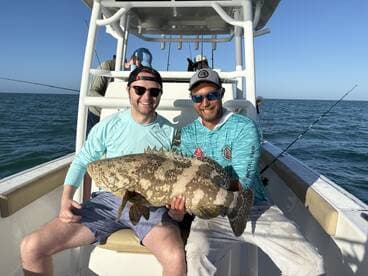 Two anglers proudly displaying a large Grouper on a fishing charter in sunny waters.