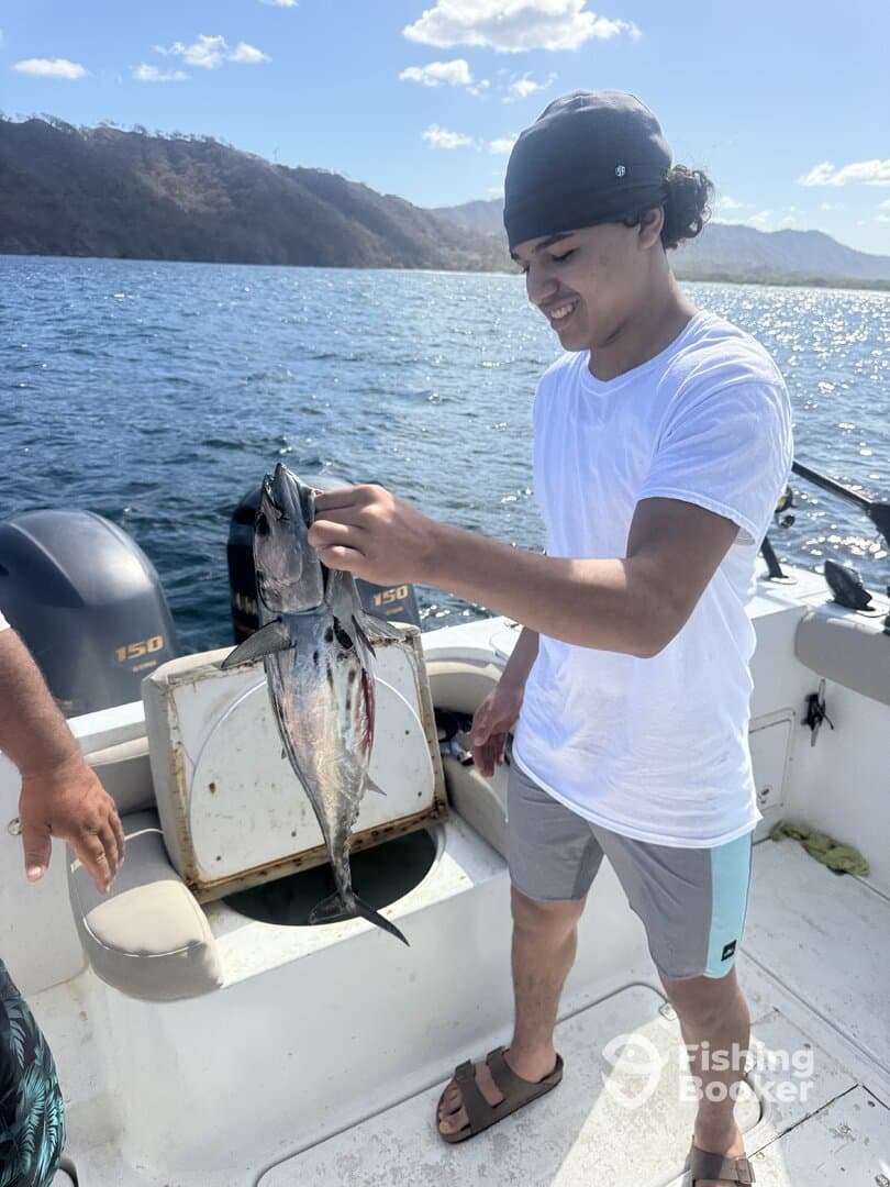 A young angler is joyfully displaying a freshly caught fish while aboard a boat in a scenic fishing environment.