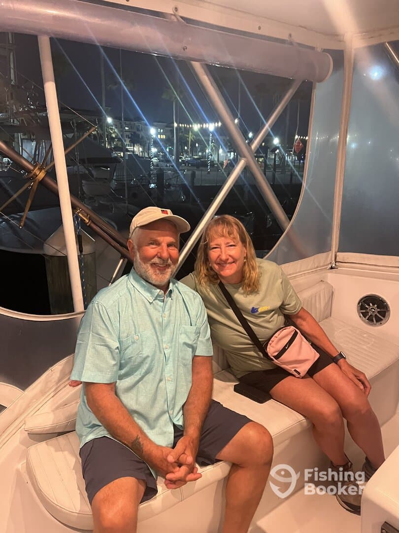 Two anglers relaxing inside the cabin of a boat, showcasing the comfortable seating and nighttime ambiance at the marina.