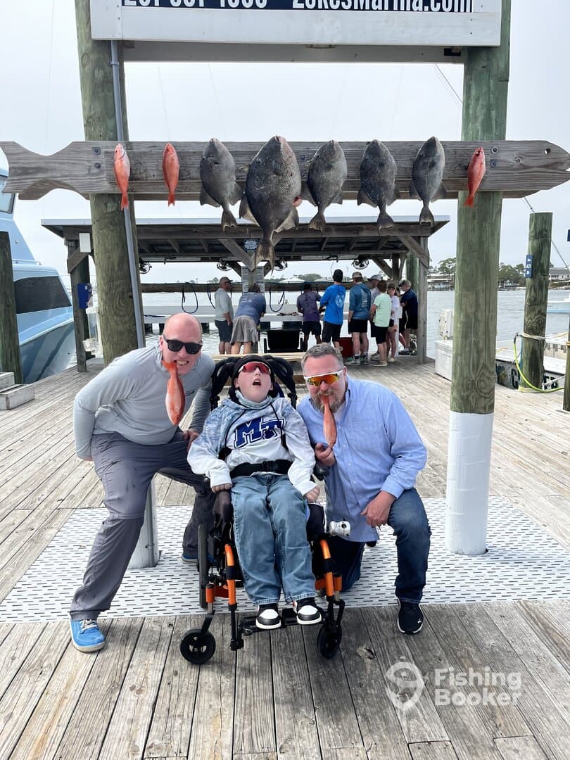 A joyful group poses with a variety of fish displayed on a board at the dock, showcasing their successful fishing trip.