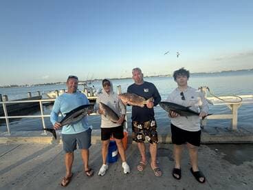 A family group proudly displaying their catch of the day, featuring multiple species of fish at the dock after a successful fishing trip.