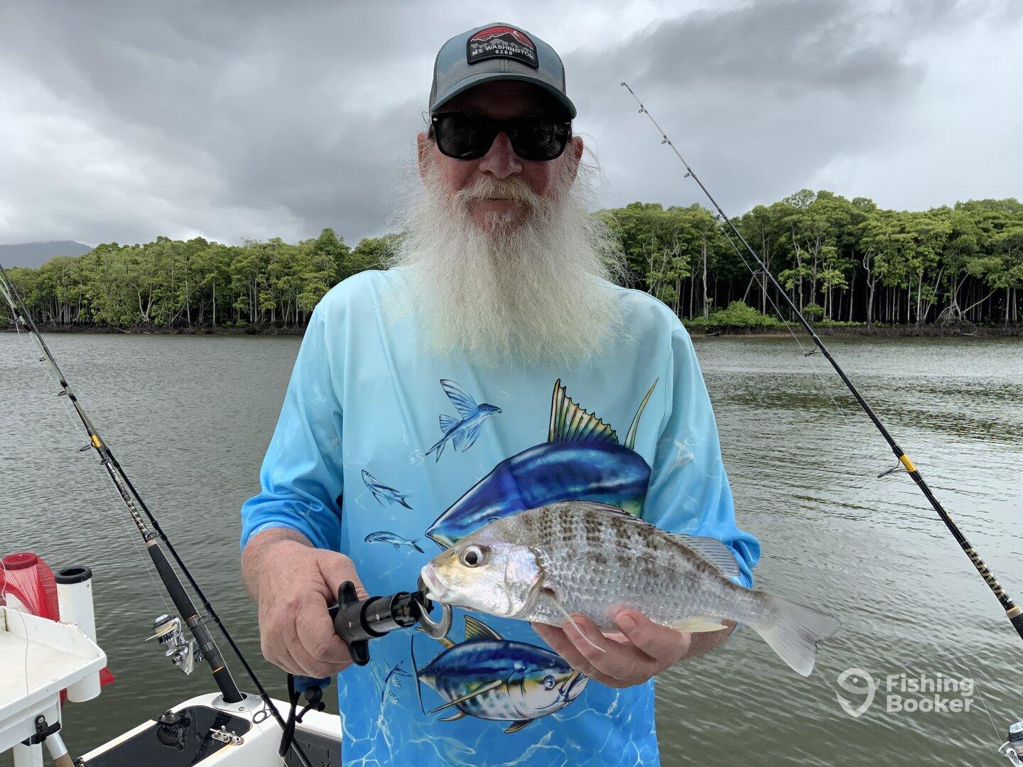 An angler proudly displaying a freshly caught fish while fishing in a scenic mangrove area.