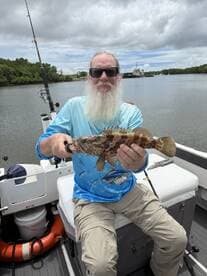 An angler proudly displaying a colorful Grouper while fishing on a boat in a scenic waterway.