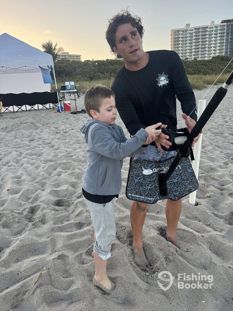 A young boy is learning to fish with an instructor on the beach, showcasing a hands-on fishing experience.