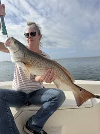 Angler proudly displaying a large Redfish while seated on a boat, showcasing a successful day on the water.