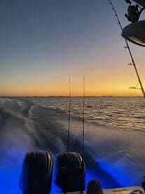 A scenic view of a boat's twin engines against a vibrant sunset, showcasing the tranquil waters and fishing rods in the background.