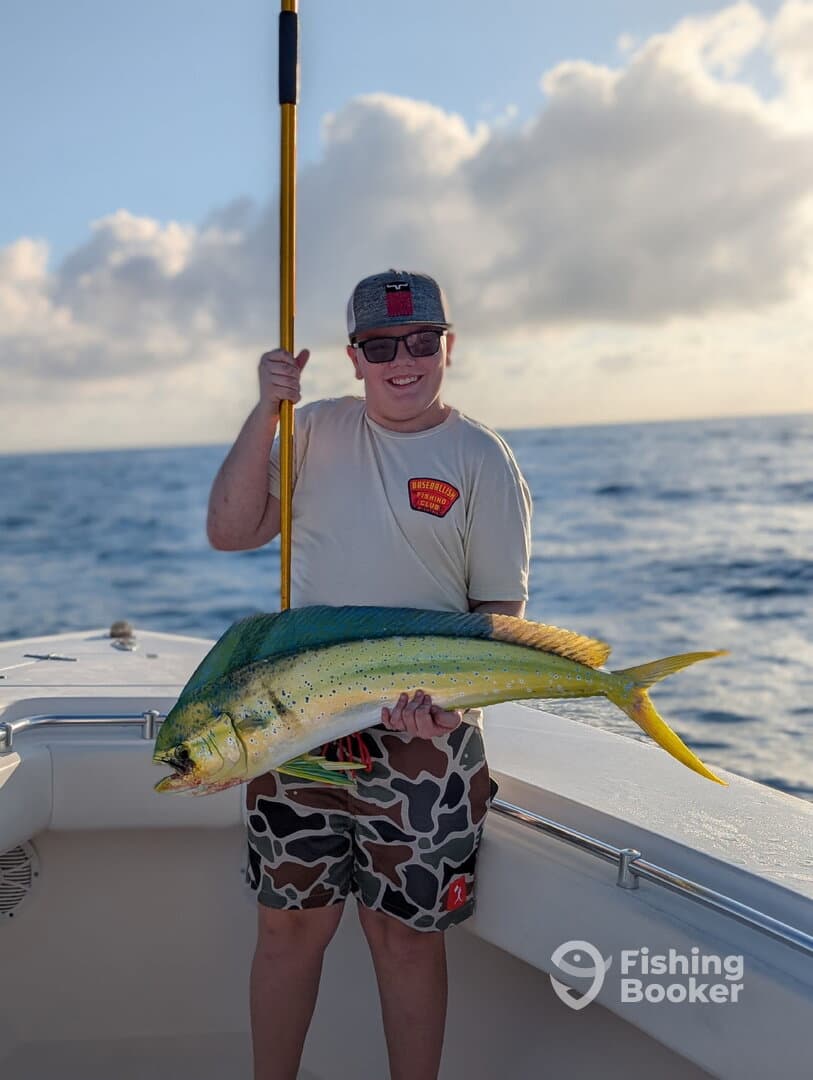 A young angler proudly displaying a vibrant Mahi Mahi while fishing offshore, showcasing a successful day on the water.