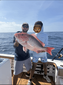 Two anglers proudly displaying a large Red Snapper on a fishing charter in open waters.