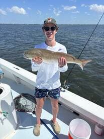 Young angler proudly holding a large Redfish while fishing on a boat in a coastal waterway.