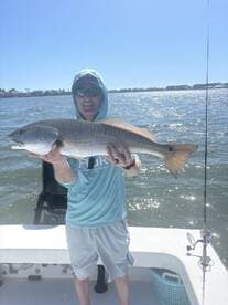 Angler proudly displaying a large Redfish while fishing on a sunny day, showcasing the excitement of a successful catch.