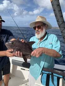 Two anglers proudly displaying a large fish while fishing in open waters, showcasing a successful day on the boat.