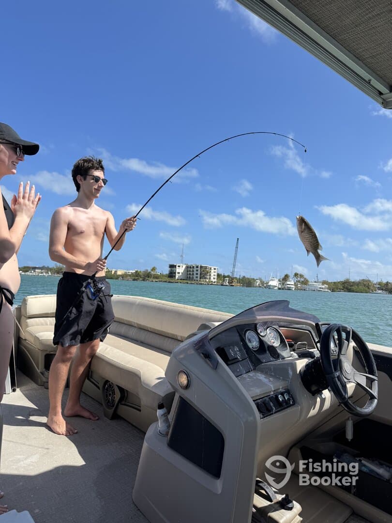 A young angler reeling in a fish while enjoying a sunny day on a boat, showcasing the excitement of fishing in a vibrant coastal setting.