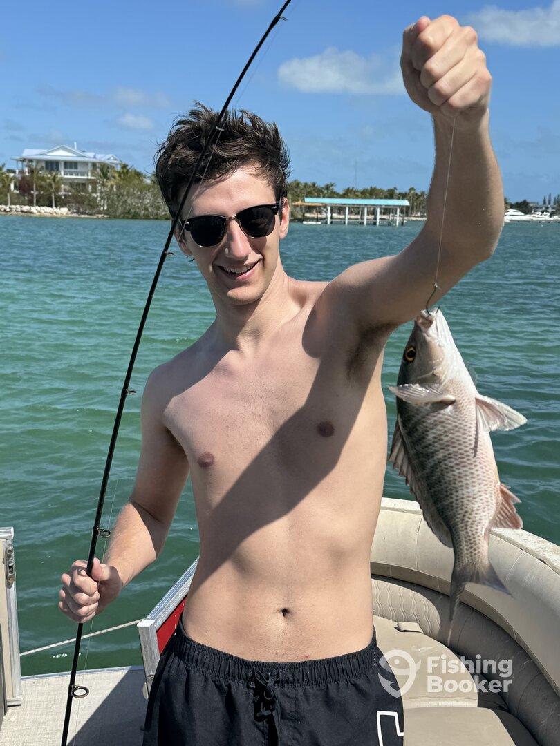 A young angler proudly displaying a freshly caught fish while fishing from a boat in a sunny coastal environment.