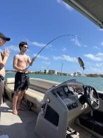 A young angler reeling in a fish while enjoying a sunny day on a boat, showcasing the excitement of fishing in a vibrant coastal setting.