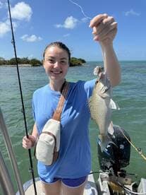 A young woman proudly displaying her catch, a small fish, while fishing off the coast in a sunny environment.