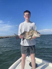 A young angler proudly displaying a large Black Drum while fishing on a boat under a clear blue sky.