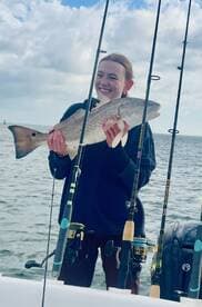 Angler proudly displaying a large Redfish while fishing on a boat, showcasing a successful day on the water.