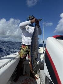 Angler proudly displaying a large Wahoo on a fishing boat in open waters, showcasing a successful deep-sea fishing trip.
