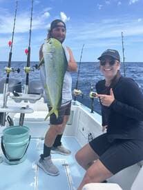 Two anglers proudly displaying a vibrant Mahi Mahi aboard a fishing boat in open waters.