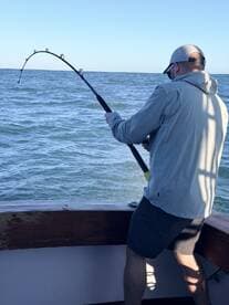 An angler actively reeling in a fish while fishing on a boat, showcasing the excitement of the catch in open waters.