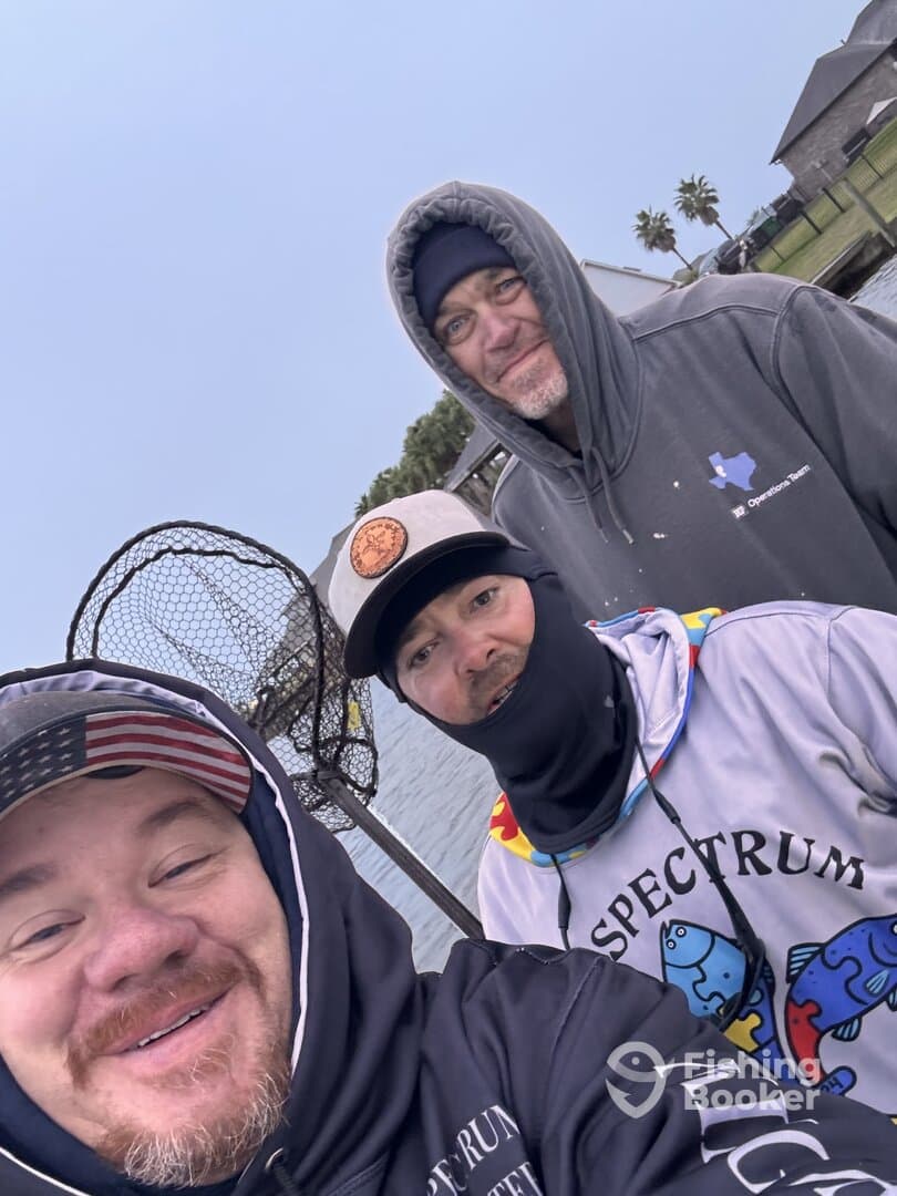 Three anglers posing for a selfie on a fishing trip, with a net visible in the background.