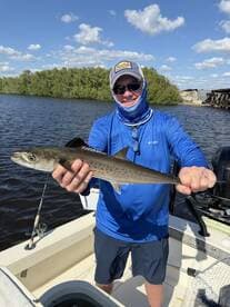 Angler proudly displaying a Speckled Trout while fishing from a boat in a scenic waterway.
