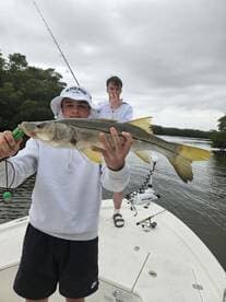 Young angler proudly displaying a Snook caught while fishing on a boat in a coastal waterway.