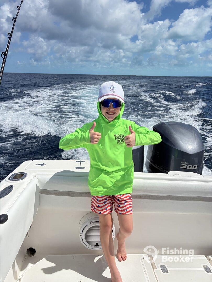 A young angler giving a thumbs up while enjoying a day on a boat, showcasing excitement for the fishing adventure.