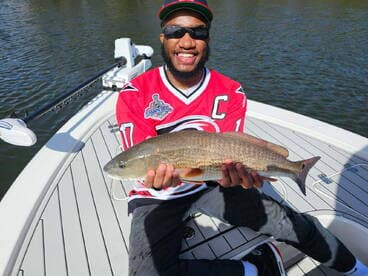 Angler proudly displaying a Redfish while standing on the deck of a boat, showcasing a successful day on the water.