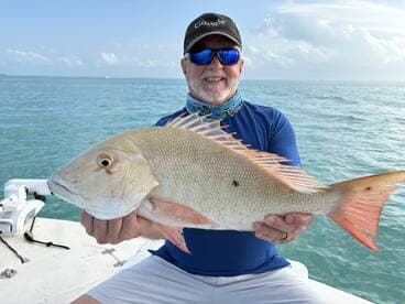 Angler proudly displaying a large Snapper while fishing in clear waters, showcasing a successful day on the boat.