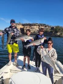 A family proudly displaying their catch of striped bass while enjoying a day on the water.