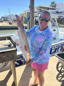A proud angler holding a large Redfish at the dock, showcasing a successful day of fishing.