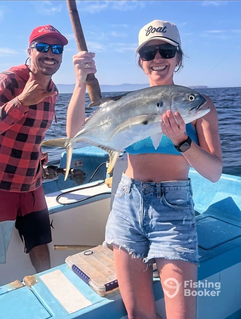 A smiling angler proudly displays a large Jack Crevalle while fishing on a boat, with a scenic ocean backdrop.